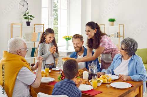 Big family has a lunch sitting at table enjoys the pie in mom\'s hands in loving room at home. Grandparents, parents and children are happy about the pie. Emotional family moments together concept.