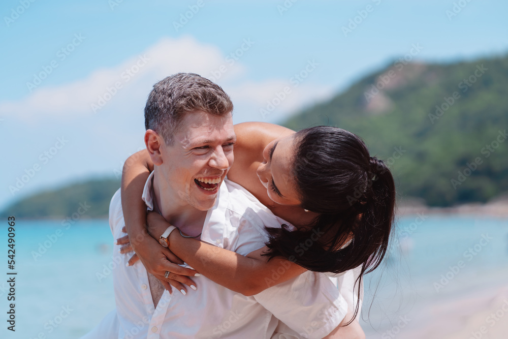 Young couple in love outdoor. Happy man giving piggyback ride to his woman and laughing at tropical beach. Girlfriend getting piggyback ride from boyfriend at sunrise in summer. Young couple in love outdoor. Happy man giving piggyback ride to his woman and laughing at tropical beach. Girlfriend getting piggyback ride from boyfriend at sunrise in summer.