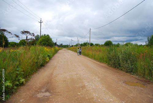 Children walk along the road in the village. Summer village landscape. Walking along a rural road. The road in the village.