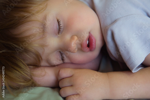 Cute sleeping baby. Children's Daytime sleeping. The Little Caucasian Boy sleeping on stomach in a big bed under a blanket. Close-up portrait of a beautiful sleeping child.