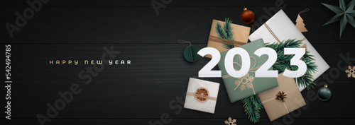Happy New 2023 Year greeting banner. Xmas Flat lay composition with fir tree branches, cinnamon, orange slice, gift craft boxes, pine cone and white numbers 2023 on black wooden floor.