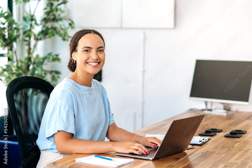 Photo of a successful confident gorgeous mixed race woman, business mentor, financial advisor, programmer, seo, sitting at a work desk in a modern office, looking at camera, smiling friendly Photo of a successful confident gorgeous mixed race woman, business mentor, financial advisor, programmer, seo, sitting at a work desk in a modern office, looking at camera, smiling friendly