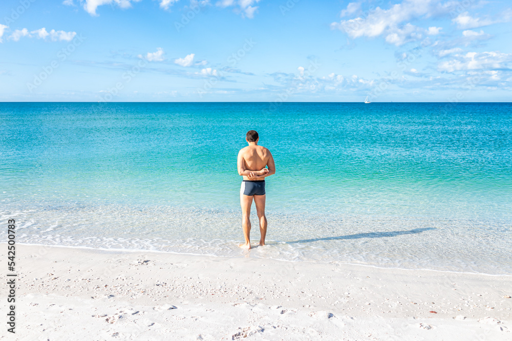Young fit muscular adult man at Barefoot beach of Bonita Springs near Naples, Florida standing swimming in clear transparent turquoise ocean sea Gulf of Mexico water with horizon