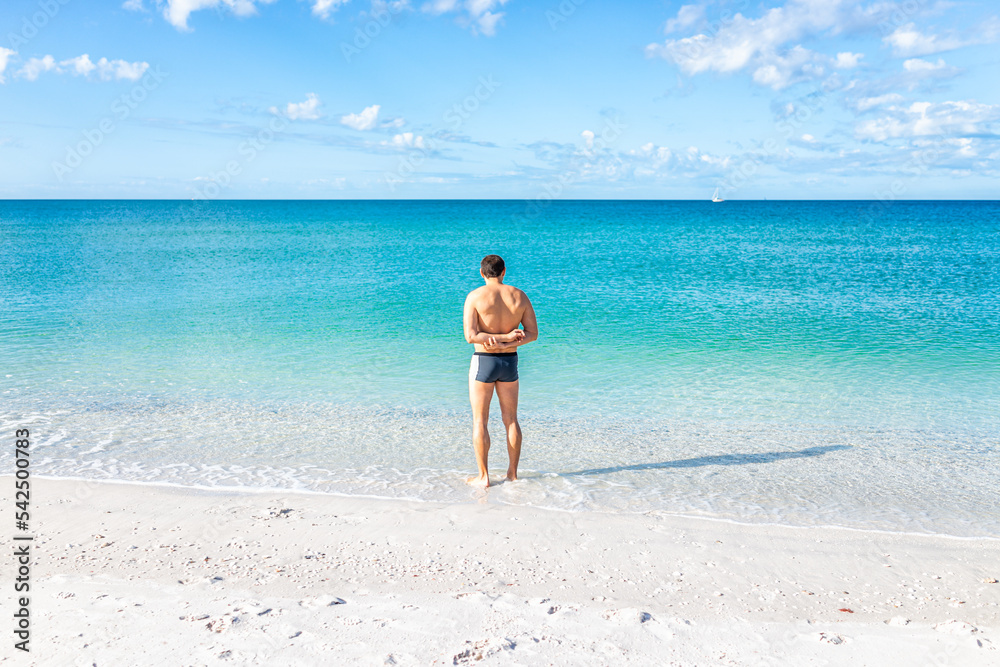 Young fit muscular adult man at Barefoot beach of Bonita Springs near Naples, Florida standing swimming in clear transparent turquoise ocean sea Gulf of Mexico water with horizon Young fit muscular adult man at Barefoot beach of Bonita Springs near Naples, Florida standing swimming in clear transparent turquoise ocean sea Gulf of Mexico water with horizon