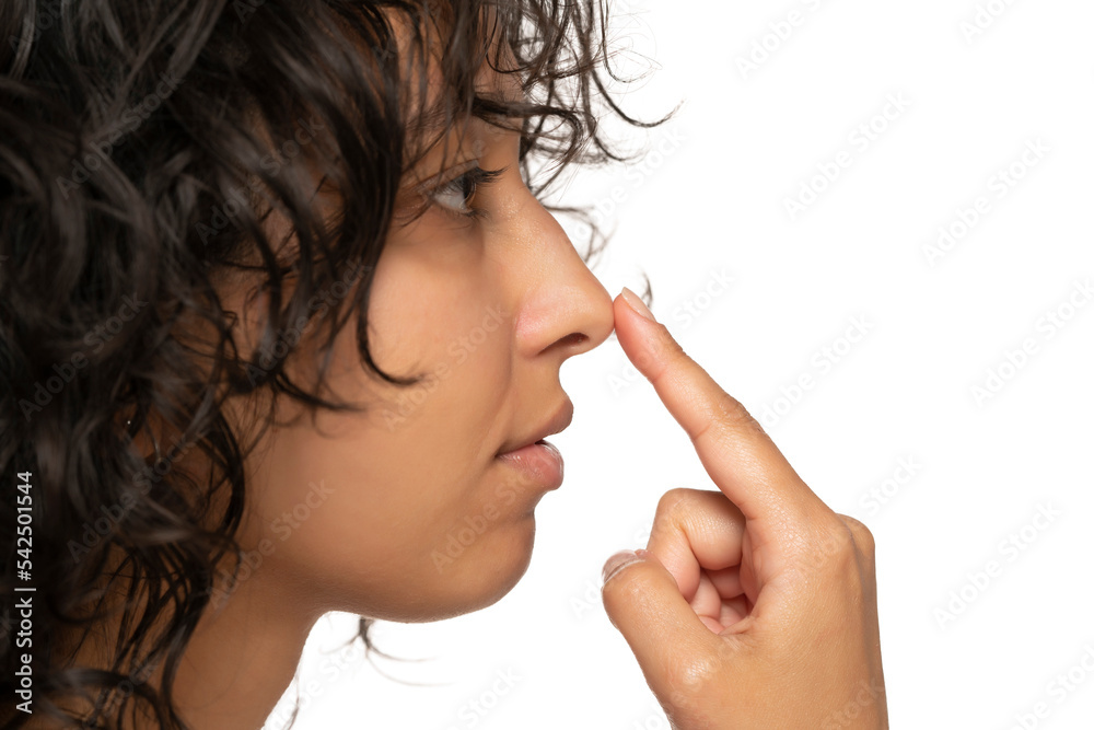 Young etnic woman touches her nose with her fingers on a white background. Side view Young etnic woman touches her nose with her fingers on a white background. Side view