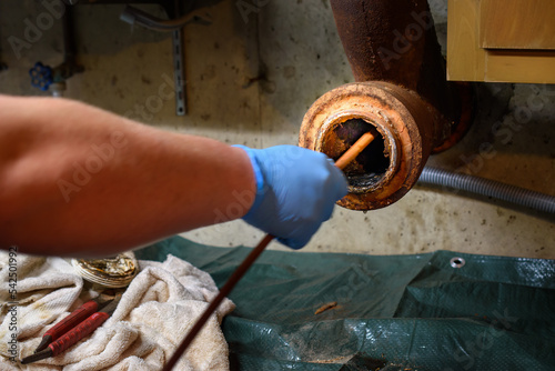Hands of a plumber as he runs a camera scope and cleaning machine through the main pipe to unclog the drain to the Septic System.  Hard-working tradesman.