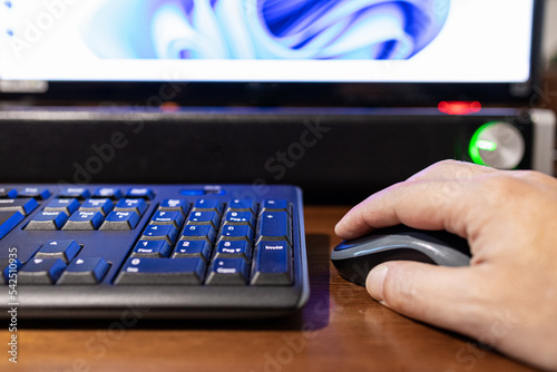 Selective focus on a hand that is clicking on a mouse with monitor and soundbar out of focus in background.