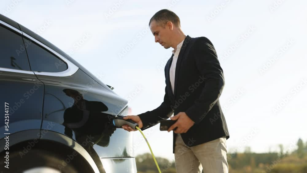 Vidéo Stock Male charging EV vehicle outdoors at sun light. Businessman