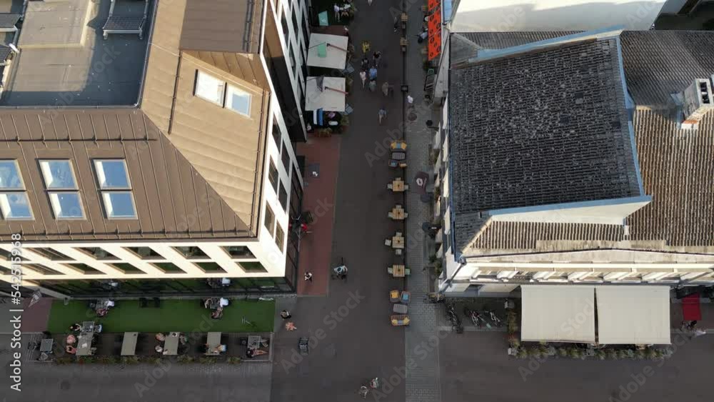 Aerial view looking down to the city center street. Drone slowly tilting up. People walking in the streets. Sunny summer day in the city urban. People walk, car, bus traffic transportation in old town Aerial view looking down to the city center street. Drone slowly tilting up. People walking in the streets. Sunny summer day in the city urban. People walk, car, bus traffic transportation in old town