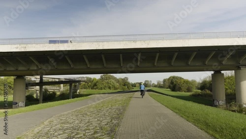 cyclist rides under a bridge while traffic passes on top of the bridge