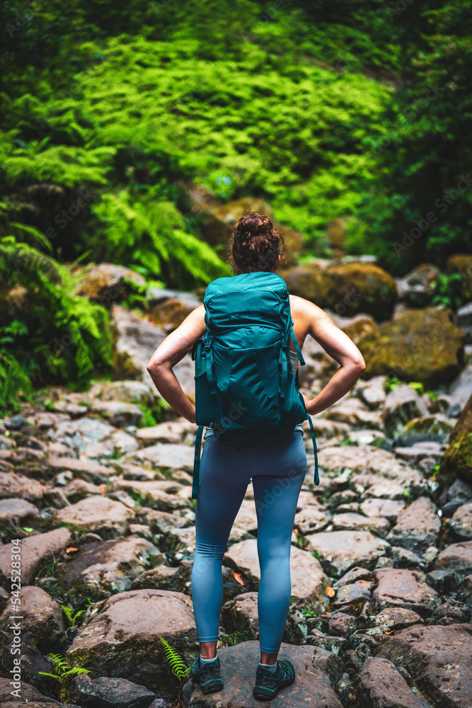 Athletic woman walks through adventurous jungle path along rocky river bed. Levada of Caldeirão Verde, Madeira Island, Portugal, Europe. Athletic woman walks through adventurous jungle path along rocky river bed. Levada of Caldeirão Verde, Madeira Island, Portugal, Europe.
