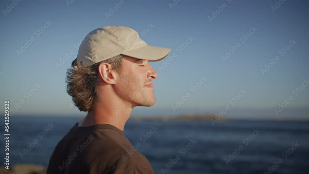 Carefree young male takes deep breath of fresh air by the ocean