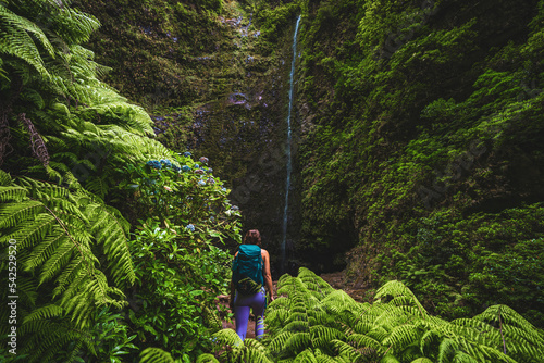 Beautiful athletic woman walks along flowery and farny trail at amazing jungle water fall. Levada of Caldeirão Verde, Madeira Island, Portugal, Europe. photo