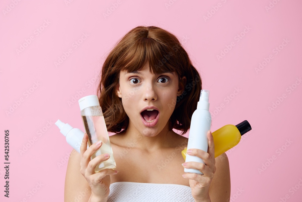 a close horizontal photo on a pink background of a shocked, surprised woman, holding various care products in her hands and looking at the camera with her mouth wide open. Skin care topics a close horizontal photo on a pink background of a shocked, surprised woman, holding various care products in her hands and looking at the camera with her mouth wide open. Skin care topics