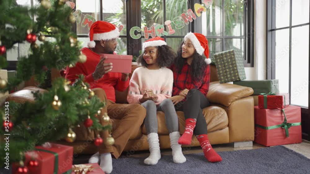 An African American black family, woman, father, mother and kid girl with present gift in party on Merry Christmas Eve Xmas on holiday. Celebration at home. People lifestyle. An African American black family, woman, father, mother and kid girl with present gift in party on Merry Christmas Eve Xmas on holiday. Celebration at home. People lifestyle.