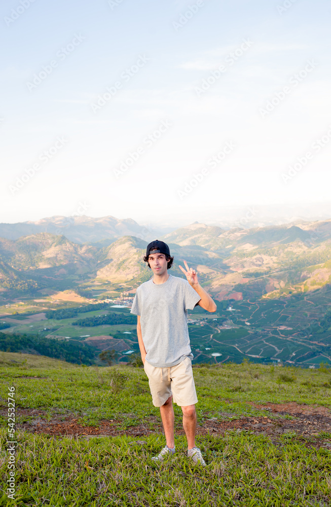 Young man standing and posing for a photo in a place with a view of a valley and mountains.