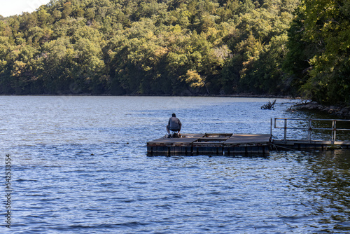 fisherman sitting on pier in lake with forest background