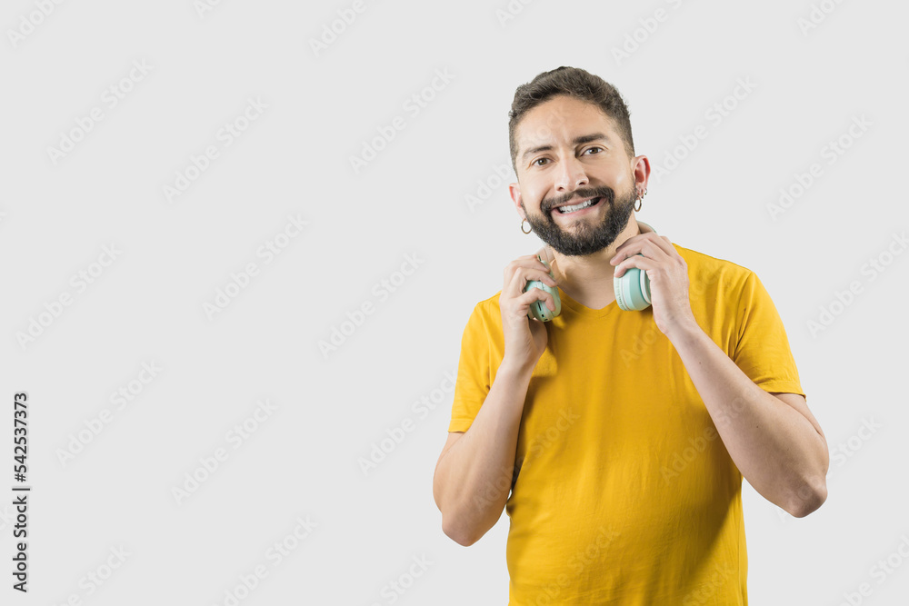 Fototapeta premium A latin adult man with yellow shirt on white background is grabbing a headphones with his two hands