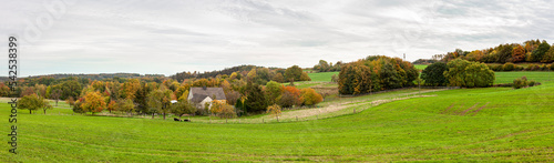 Panoramic rural autumn scenery in North Rhine Westphalia in Germany. Farm lodge in the middle of a vast green field.