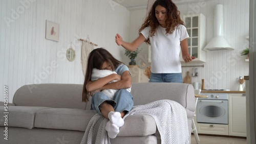 Angry mad mother waving hands and scolding sad school age daughter for bad behavior at home. Aggressive caucasian woman punishing upset teenage girl sits on sofa guilty of bad deed or disobedience