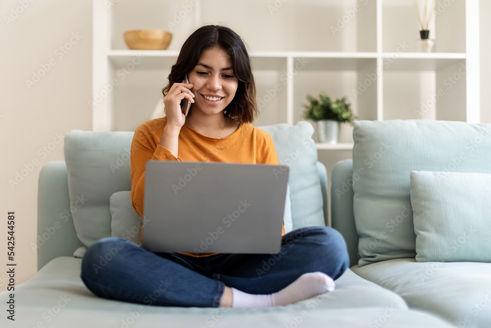 Middle Eastern Woman Using Laptop And Talking On Mobile Phone At Home Middle Eastern Woman Using Laptop And Talking On Mobile Phone At Home