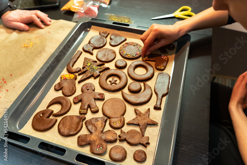 Bild auf Leinwand A woman decorates ginger cookies of different shapes, lying on baking paper on a