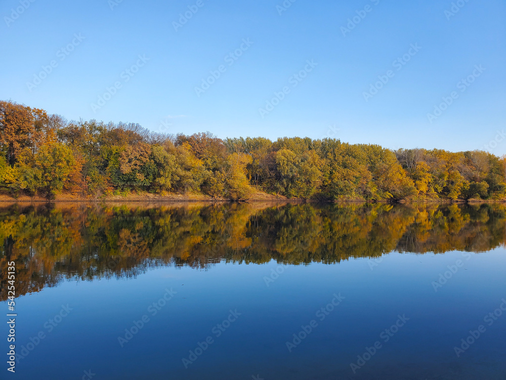 Autumn landscape with river, sky and yellow forest. yellow and orange trees of the forest are reflected in the water of a calm river or lake