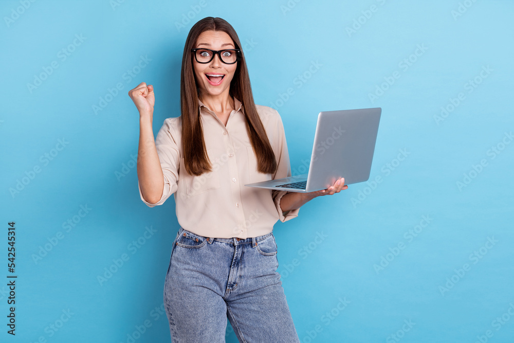 Portrait of impressed confident pretty girl dressed beige blouse jeans hold laptop screaming yeah fist up isolated on blue color background Portrait of impressed confident pretty girl dressed beige blouse jeans hold laptop screaming yeah fist up isolated on blue color background