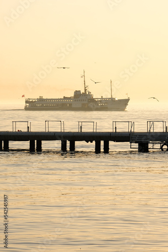 Ship passing from horizon. Golden colors on the weather and sea with ship and dock. Sea sun ship background.