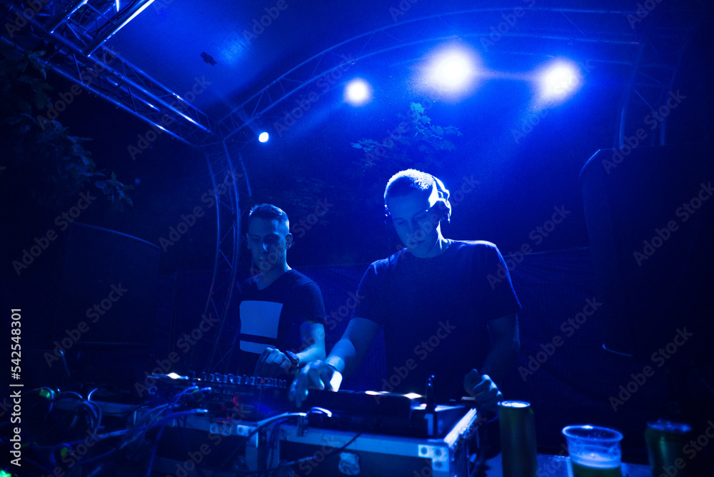 Two dj boys playing techno music on the stage at night summer concert Two dj boys playing techno music on the stage at night summer concert