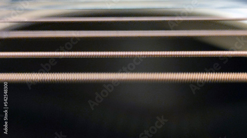 Metal guitar strings. The smooth brown surface of a guitar over which the strings are stretched. They are of different thickness, some of the strings vibrate making a sound, some are at rest.