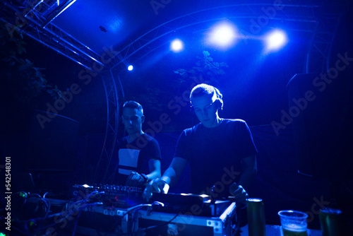 Two dj boys playing techno music on the stage at night summer concert