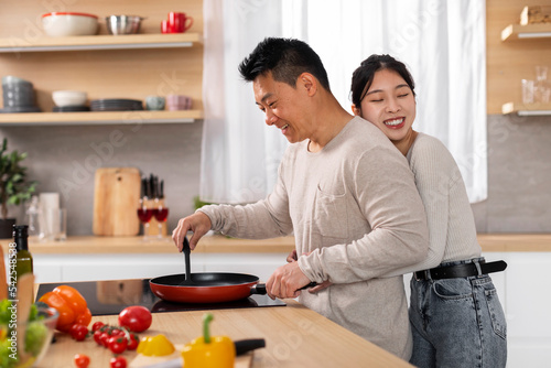 Loving asian woman hugging her boyfriend cooking meal