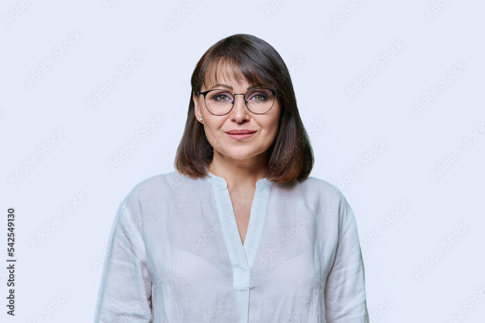 Smiling middle aged female looking at camera on light studio background Smiling middle aged female looking at camera on light studio background