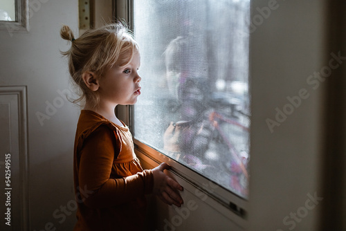 Young girl looking out from inside at the front door photo