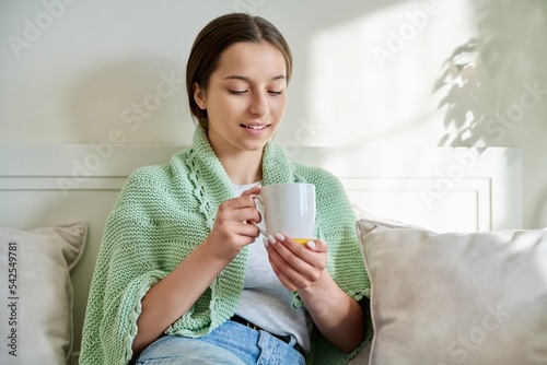 Adolescent girl resting with cup of hot tea, sitting on couch at home