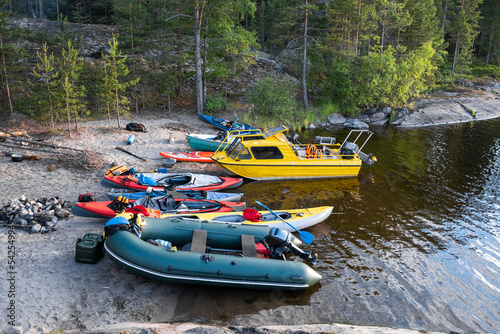 Tourist kayaks and a yellow boat in a rocky and wooded bay of the lake. Equipment is scattered around the boats on the shore