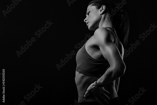 Sporty woman holding hands to relax the tension and pain in lower back and sacrum in sport top on empty copy space studio background. Back view. The concept of medicine. photo