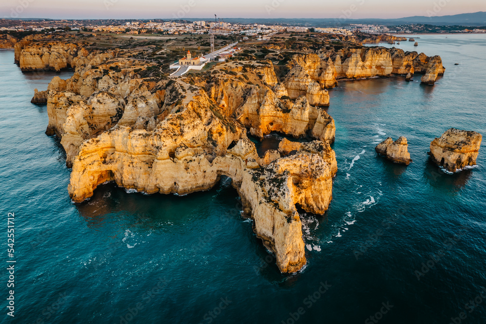Coastal golden cliffs at sunrise in Ponta da Piedade near Lagos,Portugal.Spectacular rock formations with caves,and sea arches,lighthouse.Summer vacation by Atlantic Ocean.Famous beach in Algarve