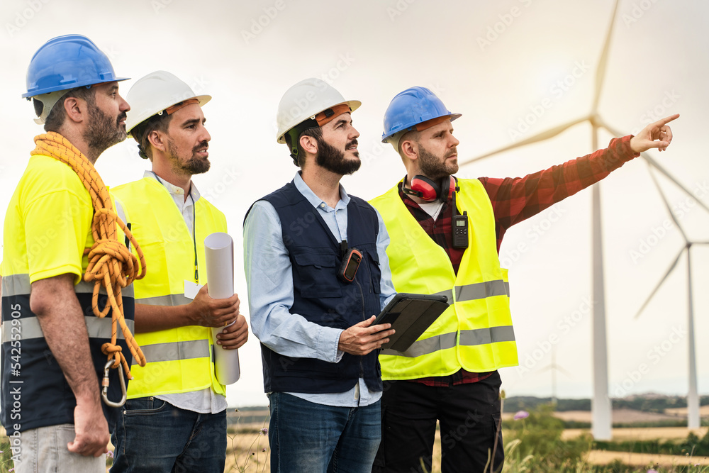 Professional workers working in front of windmill Electricity station. Back view of Civil Engineer and electricians discussing about projects Professional workers working in front of windmill Electricity station. Back view of Civil Engineer and electricians discussing about projects