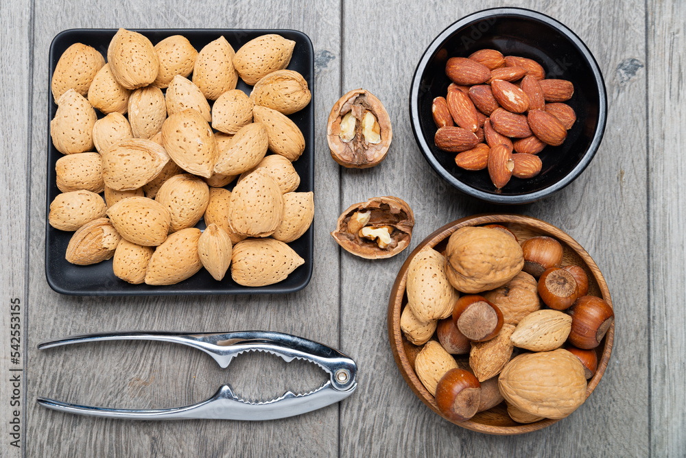 nuts in bowls and a nutcracker on a gray table. top view, Assortment of nuts - cashew, hazelnuts, almonds, walnuts, pistachio, pecans, pine nuts, peanut. nuts in bowls and a nutcracker on a gray table. top view, Assortment of nuts - cashew, hazelnuts, almonds, walnuts, pistachio, pecans, pine nuts, peanut.