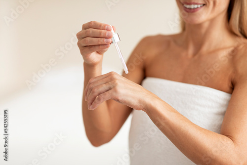 Middle aged woman applying anti-aging serum on her hand, making beauty routine after bath © Prostock-studio