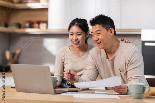 Positive asian couple paying for goods and services on Internet