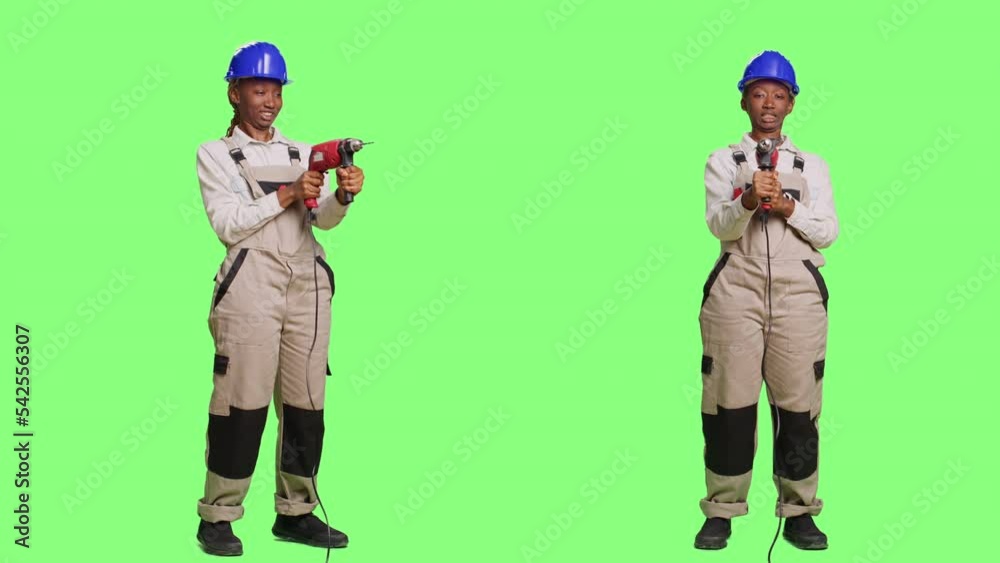 Female contractor in uniform and hardhat holding power drill or nail gun over full body green screen backdrop. Using drilling gun to renovate and redecorate, wearing overalls and helmet. Female contractor in uniform and hardhat holding power drill or nail gun over full body green screen backdrop. Using drilling gun to renovate and redecorate, wearing overalls and helmet.