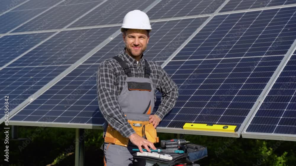 Male engineer in protective helmet installing solar photovoltaic panel system using screwdriver. Electrician mounting blue solar module on roof of modern house. Alternative energy ecological concept Male engineer in protective helmet installing solar photovoltaic panel system using screwdriver. Electrician mounting blue solar module on roof of modern house. Alternative energy ecological concept