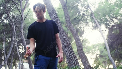 Young male practicing kendama moves in the woods.