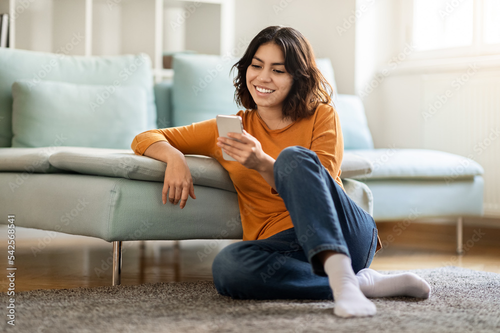 Obraz premium Smiling Young Arab Lady With Smartphone Relaxing On Floor At Home