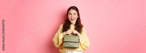 Thoughtul beautiful woman smiling, looking aside at upper left corner with pleased face, imaging something, having an idea, standing over pink background photo