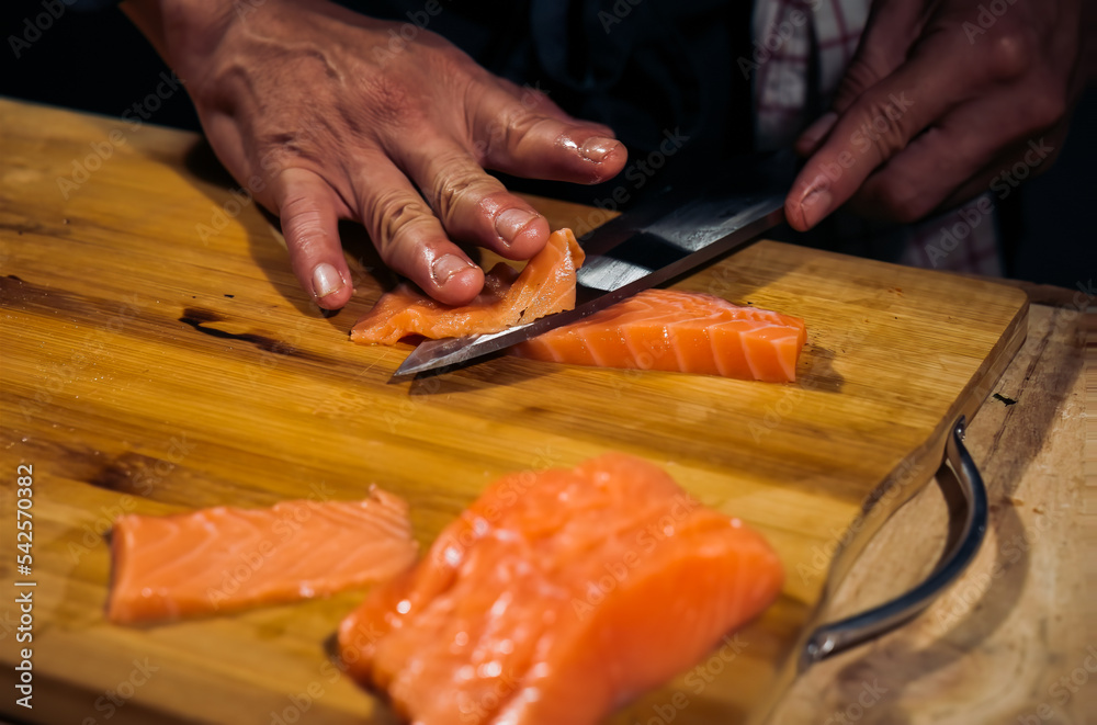 Close up of Chef cook hands chopping salmon fish for traditional Asian cuisine with Japanese knife. Professional Sushi chef cutting seafood japanese chefs are making salmon fish sashimi. dark tone
