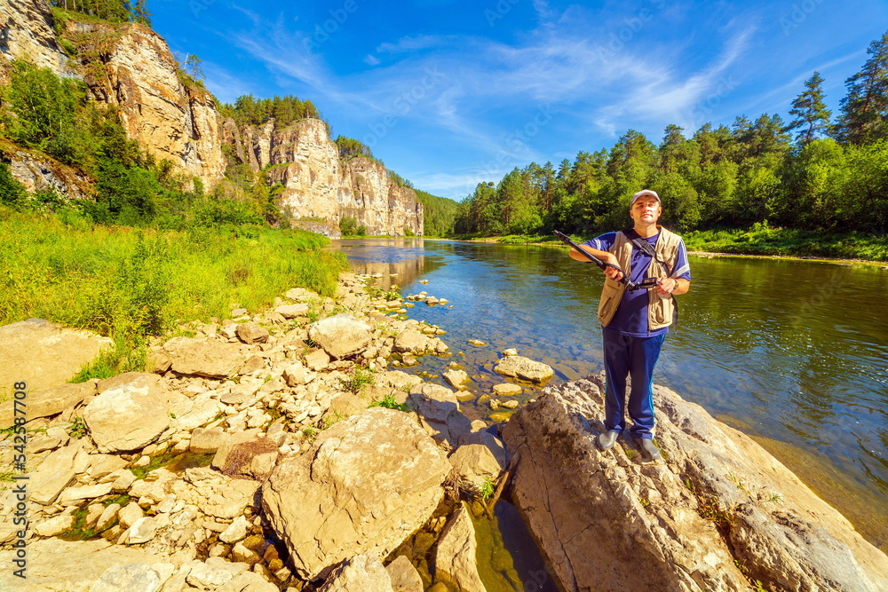 a young handsome man tourist on the bank of the Ai River against the backdrop of the Aisky cliffs on a sunny summer day.